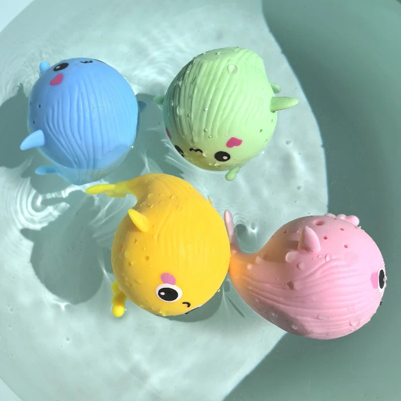 Cuatro ballenitas de baño flotando en el agua: azul, verde, amarilla y rosa