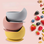 Bowls de silicona con ventosa apilados en gris, rosa y amarillo junto a frutas