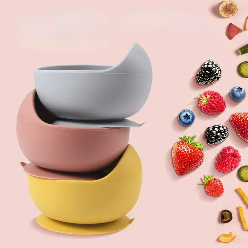 Bowls de silicona con ventosa apilados en gris, rosa y amarillo junto a frutas