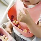 Bebé comiendo en su silla con el babero de silicona con bolsillo recogemigas