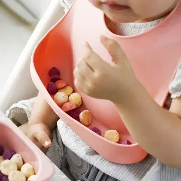 Bebé comiendo en su silla con el babero de silicona con bolsillo recogemigas